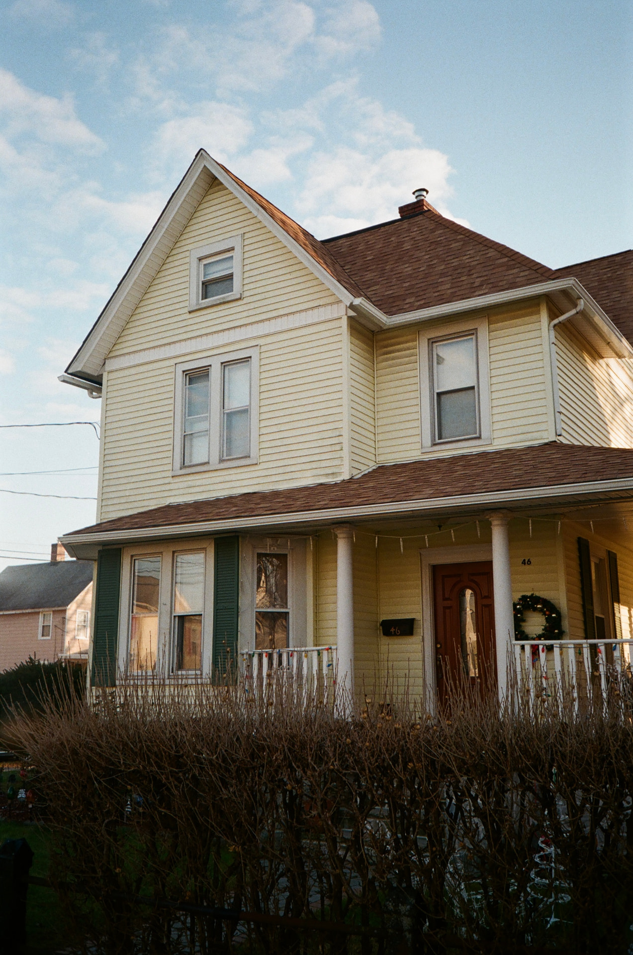A pale yellow two-story house with a covered porch in Dover, New Jersey at golden hour