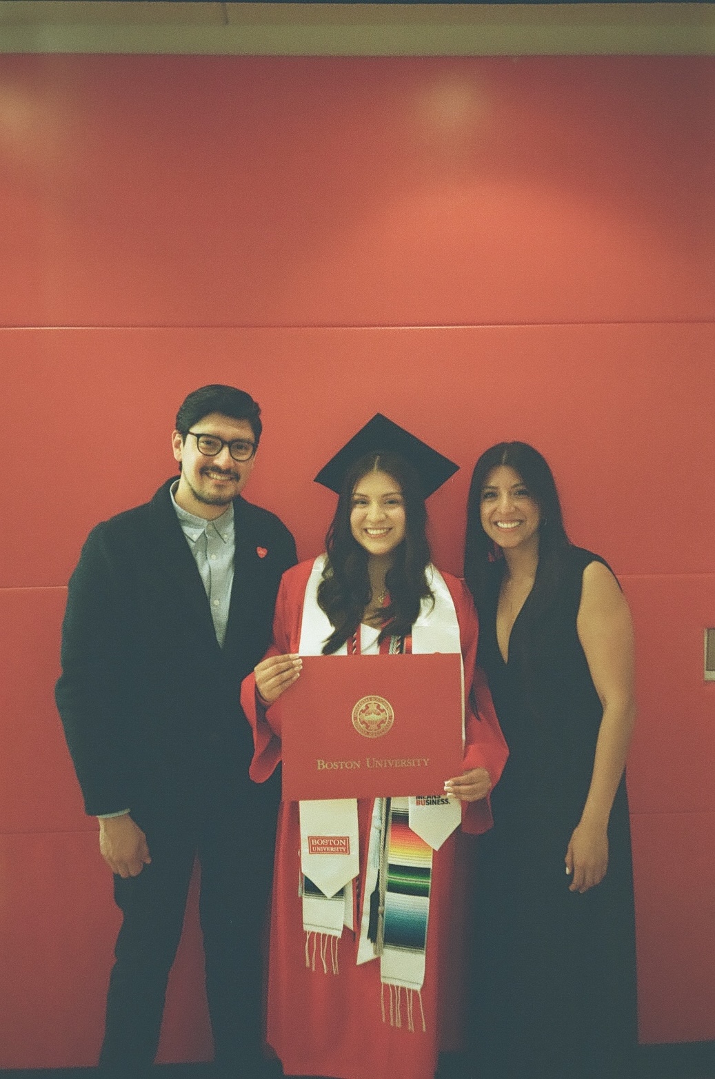 Family graduation photo at Boston University against a red wall